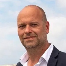Een portretfoto van Michel Aaldering, de directeur VVV Terschelling. De foto is is vanaf de schouders genomen. Michel staat tegen een achtergrond van een bewolkte lucht en glimlacht in de camera.